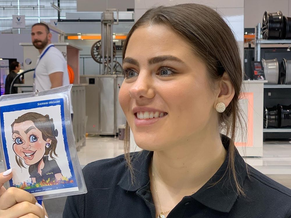 Eine junge Frau hält ihre fertige iPad-Karikatur auf der Paint Expo Messe in Karlsruhe neben sich und präsentiert stolz das Ergebnis.