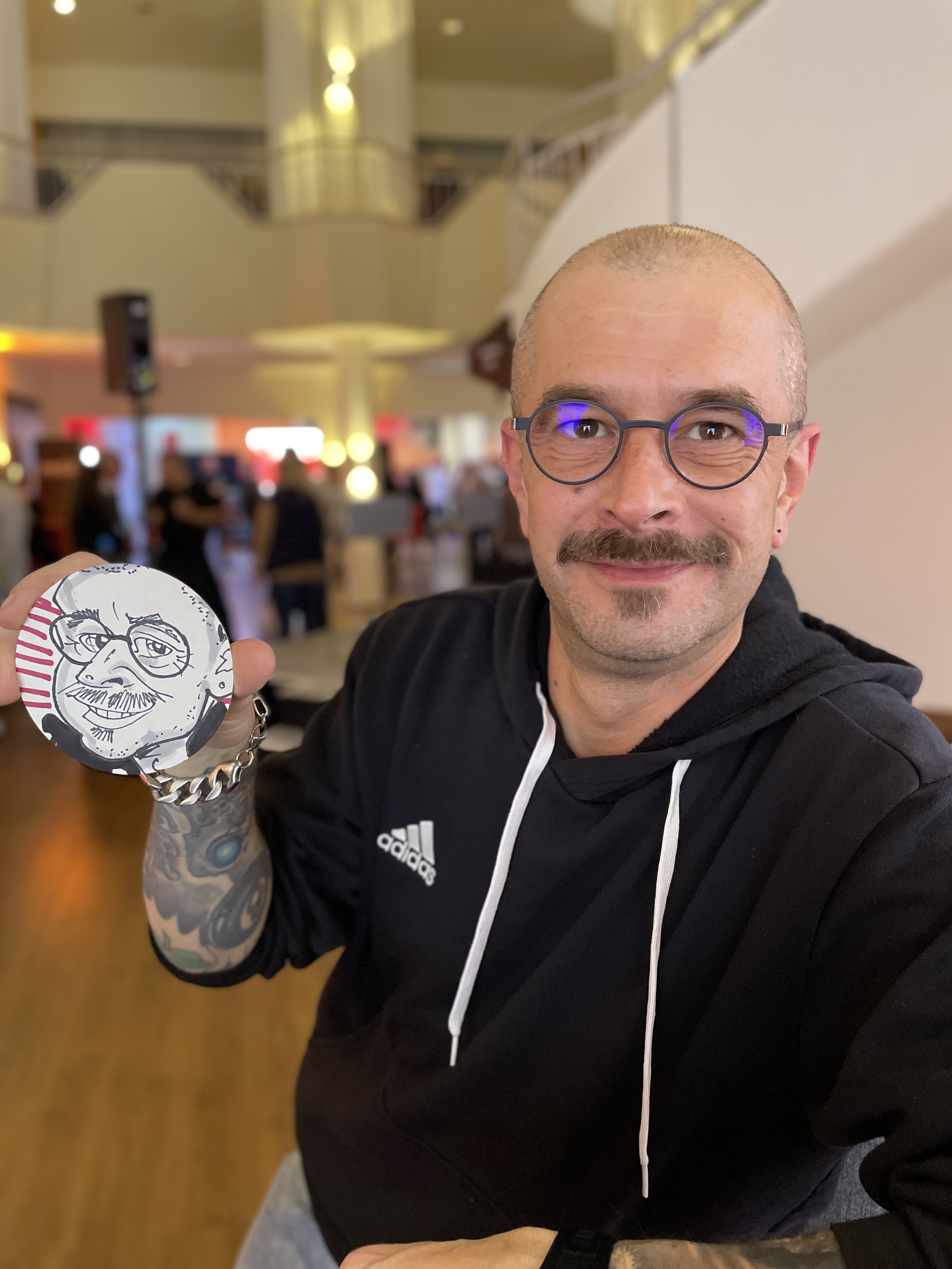 Ein Mitarbeiter hält seine Bierdeckel-Karikatur von Bierdeckelzeichner Erol in die Kamera