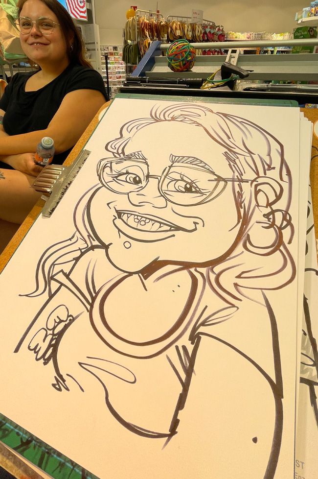 Eine junge Frau lässt sich von Erol klassisch auf Papier zeichnen. Aufgenommen in der Pfalz in einem dm-Drogeriemarkt.